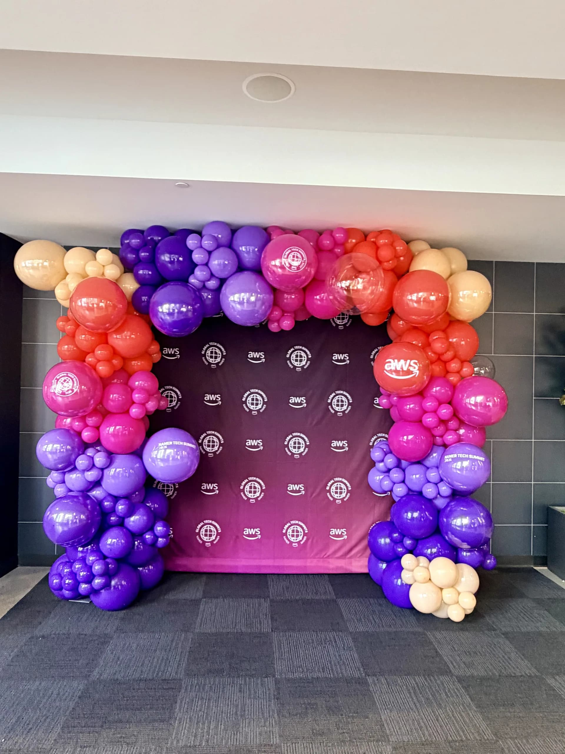 Two statement balloon arches and a branded photo zone for AWS at the Tech Summit 2026 in San Francisco, California.
