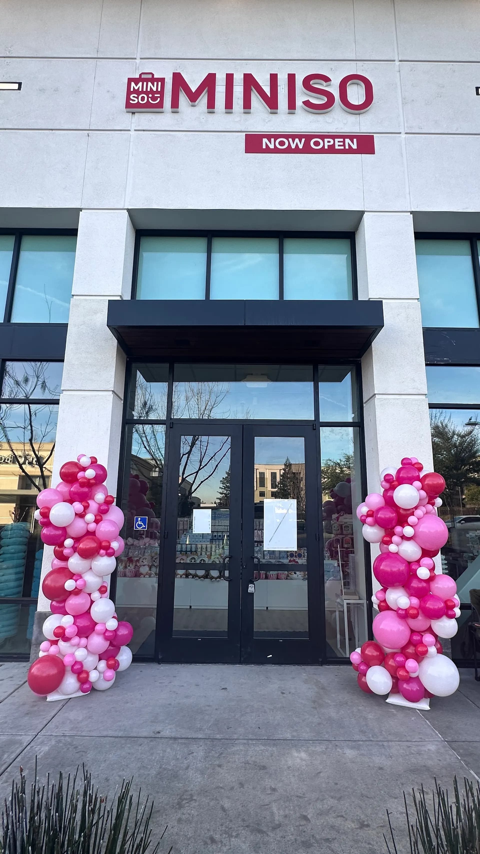Red and white branded entrance balloon columns installed for a MINISO store grand opening in the San Francisco Bay Area.